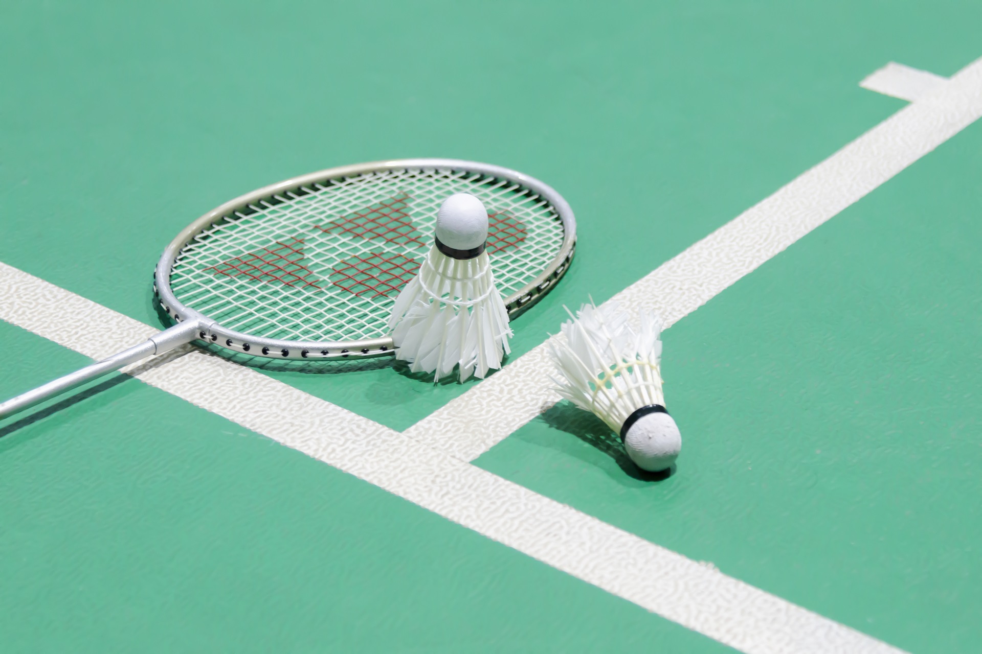 White,Badminton,Shuttlecock,On,A,Green,Floor,With,Blurred,Players